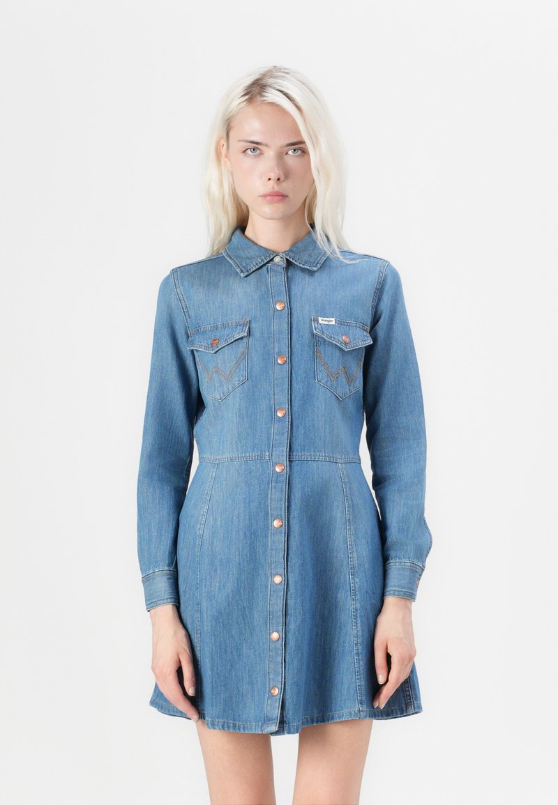Denim dress with a collar, long sleeves, and button front. Features two chest pockets with contrasting stitching and a flared hem. Light blue color.