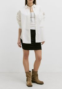 Witte blouse met knopen over een aansluitende zwarte geribde minirok, gecombineerd met beige enkellaarsjes met riempjes en een lage hak.