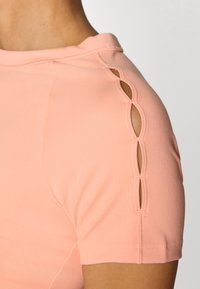 Rosa Kurzarmshirt mit auffälligen Ausschnittdetails an den Schultern, aus einem weichen, dehnbaren Material mit flachen Nähten.