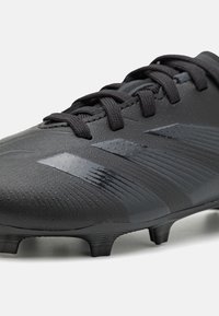 Botín de fútbol negro con superficie texturizada, material sintético, diseño con cordones y tachuelas negras; presenta franjas de acento brillantes.