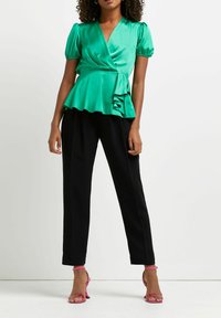 Grön satinlångärmad topp med puffärmar och volangslut; matchad med svarta byxor och rosa remsandaler. Slät textur, strukturerad design.