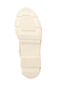 Zool van een beige schoen met textuur gripgebieden, rechthoekige en ronde patronen, maat 39 gemarkeerd, en merknaam "Travelly" in relief.