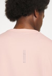 Helles Rosa T-Shirt mit rundem Halsausschnitt und einem subtilen doppellinigen Grafikdesign auf der Rückseite. Glatte Stofftextur. Lässiges Design.
