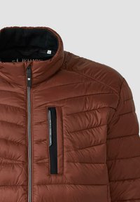 Bruine geïsoleerde jas met een hoge kraag, frontzipper en een horizontaal gestikt patroon. Beschikt over een borstzak met een zwarte accenten.