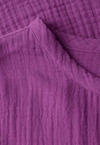 Lila texturerad tyg som visar ett rynkat mönster med en mjuk, vävd yta och har en vikt kant.
