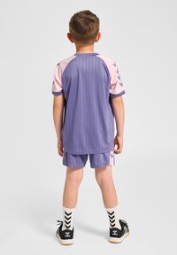 Lila sportigt outfit med vertikala ränder, rosa ärmar och matchande shorts. Inkluderar svarta skor och vita strumpor med svart chevronmönster.