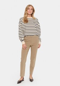 Haut à manches longues rayé crème et marine, pantalon beige cintré, et ballerines marron foncé. Tissu doux, coupe décontractée et détails minimaux.