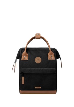 Schwarzer Stoffrucksack mit braunen Ledergriffen, Boden und Reißverschlusslaschen, Frontreißverschlusstasche und rundem Logo-Patch in der Mitte.