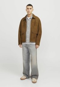 Brown suede jacket with two front pockets, layered over a black and white checkered shirt, paired with light gray wide-leg jeans and sneakers.