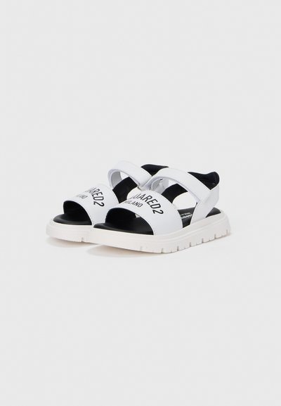 Λευκά αθλητικά σανδάλια με μαύρες λεπτομέρειες, ρυθμιζόμενους ιμάντες και παχιά λευκή σόλα με ανάγλυφο πέλμα. Διαθέτουν λογότυπο στα λουριά.