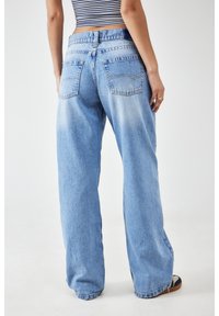Jeans de tiro alto de pierna ancha en azul claro, hechos de denim, con bolsillos traseros y áreas desgastadas para un aspecto desgastado.