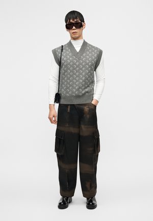 Γκρι πλεκτό γιλέκο με διακοσμητικά σχέδια πάνω από λευκό πουκάμισο μακρυμάνικο, συνδυασμένο με σκούρο παντελόνι cargo με τσέπες, ολοκληρωμένο με μαύρα παπούτσια.