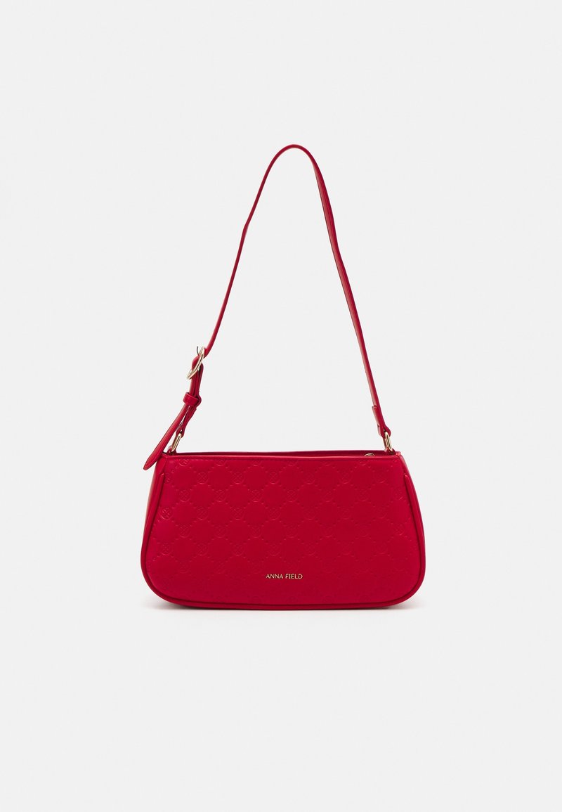 Sac bandoulière rouge en cuir texturé avec une forme courbée. Dispose d'une longue sangle et d'un logo discret en or en bas.