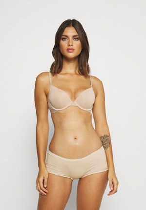 Reggiseno beige senza cuciture con ferretto e spalline regolabili abbinato a pantaloni boyshort beige, che mostravano un materiale liscio e un design semplice.