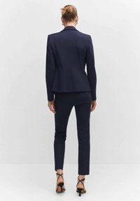 Granatowy garnitur z dopasowaną marynarką i slim-fit spodniami. Tekstura materiału wydaje się gładka, z wyraźną strukturą i minimalnymi akcentami. Widok od tyłu.