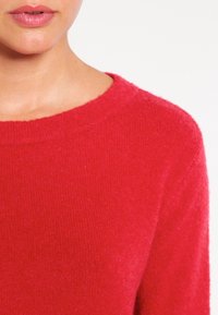 Czerwona dziergana swetra z okrągłym dekoltem, o delikatnej fakturze i gładkim wykończeniu, prezentująca żywy odcień i bez widocznych wzorów czy motywów.