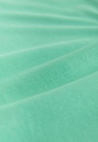 Nærbillede af glat, lyse turkis stof med bløde folder og fin strikket struktur.