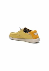 Zapato de lona amarillo con acabado texturizado, acento de talón de ante marrón y suela de goma. Cuenta con cierre de cordones y forro con patrón.