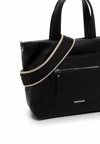 Mustast tekstureeritud nahast käekott lühikeste käepidemete ja eemaldatava beezikattega punutud rihmaga. Sisaldab esipoolset lukuga taskut.