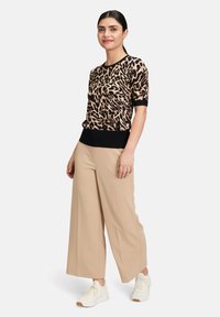 Beżowo-czarny top w zwierzęcy wzór z krótkimi rękawami i czarnym wykończeniem. Połączony z jasnobeżowymi spodniami typu wide-leg i białymi sneakersami.