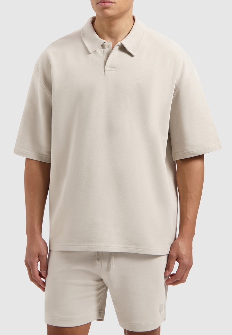 Beige poloshirt met een kraag, korte mouwen en een relaxte pasvorm. Voorzien van subtiele branding op de borst. Gemaakt van een katoenmix.