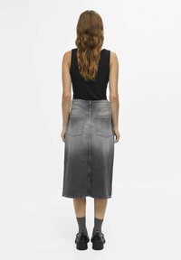 Sort ærmeløs top parret med en grå denim midi-nederdel med to baglommer og en rå kant, båret med mørke sko og grå sokker.