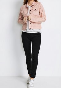 Ljus rosa denimjacka med två bröstfickor, svarta knappar och en figursydd design, matchad med svarta skinnyjeans och vita sneakers.