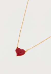 Privjesak u obliku crvenog srca na ogrlici od zlatnog lanca. Privjesak je sjajan s glatkom teksturom, u obliku zaobljenog srca.