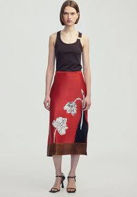 Een rode zijden rok met witte bloemenprint, een donkerblauwe accent en een bruine zoom, gecombineerd met een zwarte geribbelde tanktop en gespenhakken.