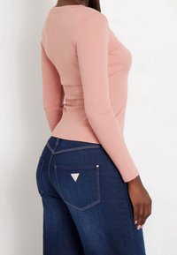 Haut en maille côtelée à manches longues de couleur rose doux, coupe ajustée. Associé à un pantalon en denim bleu foncé taille haute avec un logo triangulaire sur la poche arrière.