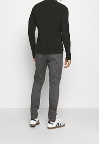 Ciemnozielona koszula z długim rękawem o fakturowanym wzorze, zestawiona z szarymi spodniami i białymi trampkami z czarnymi paskami i brązowymi podeszwami.