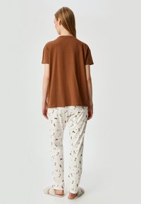 Bruine katoenen t-shirt met korte mouwen, gecombineerd met witte pyjamabroek met een speelse print van huishoudelijke artikelen. Zachte slippers maken de look compleet.