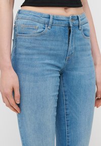 Šviesiai mėlyni džinsai su aptemptu dizainu, penkiomis kišenėmis ir užtrauktuku. Pagaminti iš denim medžiagos su lygiu tekstūru ir subtiliu nusidėvėjimu.