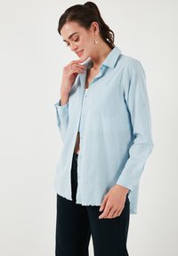 Camicia button-up azzurro chiaro con taschino, maniche lunghe e orlo grezzo. Realizzata in un tessuto leggero, presenta una vestibilità rilassata.