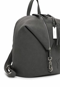 Sac à dos en cuir perforé gris foncé avec fermeture éclair argentée, détail pompon et étiquette métallique de marque sur fond blanc.
