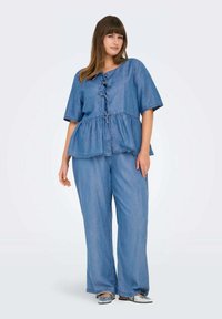 Denim peplum majica s kratkim rukavima, s vezanjem sprijeda. Uparena s odgovarajućim širim trapericama i sjajnim srebrnim cipelama na sklizak.