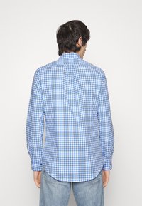 Blå och vit rutig skjorta med klassisk krage, långa ärmar och rundad nederkant. Tyget verkar smidigt och lätt.