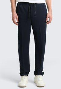 Marineblauwe trainingsbroek met een aantrekkoord in de taille, taps toelopende pijpen en een gestructureerde stof. Gecombineerd met witte sneakers met een rubberen zool.