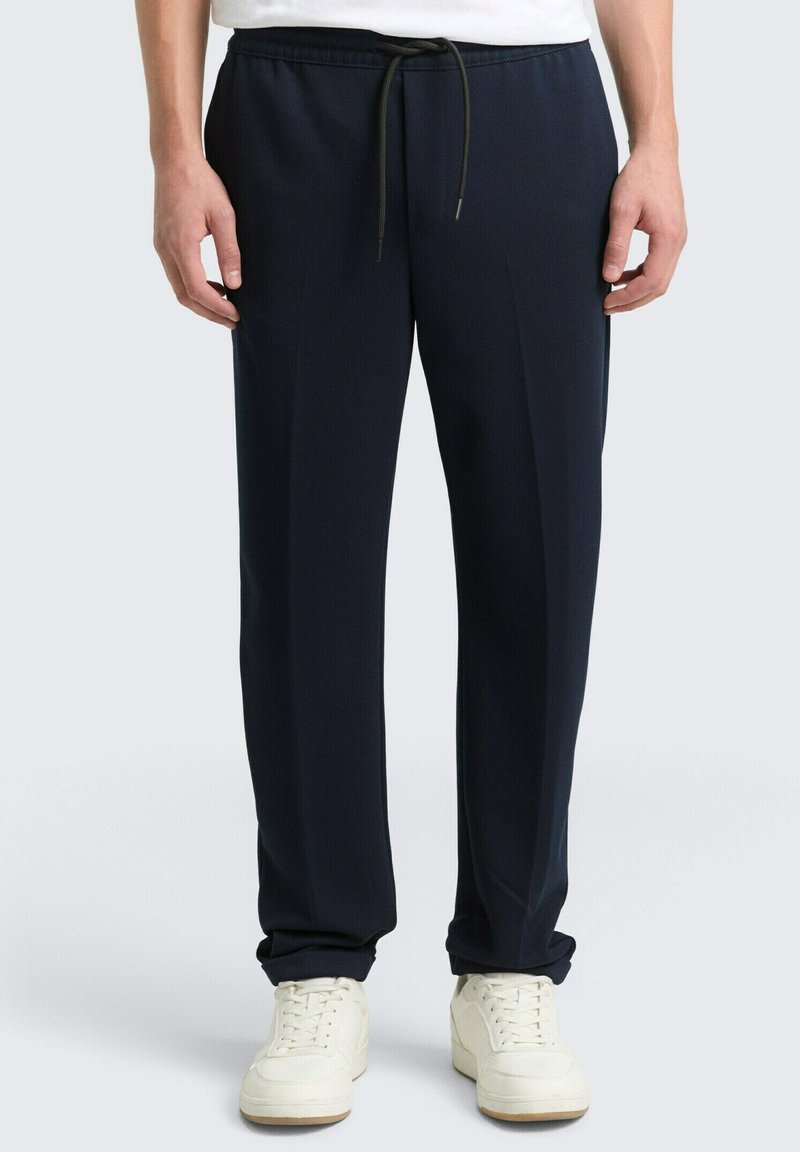 Marineblauwe trainingsbroek met een aantrekkoord in de taille, taps toelopende pijpen en een gestructureerde stof. Gecombineerd met witte sneakers met een rubberen zool.