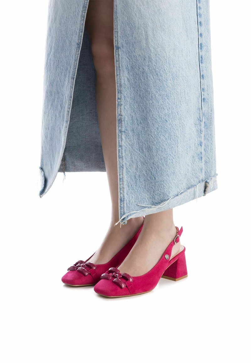 Tacones slingback de ante fucsia con punta afilada, que presentan dos detalles de lazo y un tacón grueso. Combinados con una falda de mezclilla azul clara.