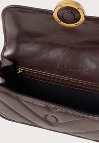 Bolsa de mão de couro marrom acolchoado aberta para mostrar o bolso interno com fecho de zíper, fecho magnético e "couro genuíno" estampado na aba interna.