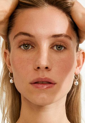 Hõbedast rõngakujulised kõrvarõngad kuuliga ripatsiga, mida kannab helenaha inimene, kellel on pikad, sirged, blondid juuksed. Loomulik meik.