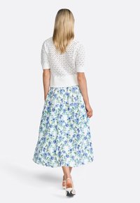 Hvid strikket top med korte ærmer og hulmønster, parret med en knælængde nederdel med blå blomstermønster på en lys baggrund.