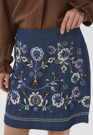 Jupon en denim orné de broderies florales multicolores en bleu, blanc et marron. Design court avec une coupe droite et un ourlet décoratif.
