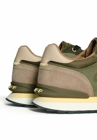 Sneaker verde e beige in pelle e suede, con un pannello testurizzato, dettagli gialli e una suola imbottita con il logo.