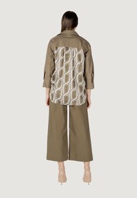 Camicia oversized verde oliva con retro a fantasia beige e bianco. Pantaloni a gamba larga verde oliva. Tacchi nudi trasparenti e appuntiti completano l'outfit.