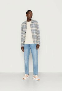 Grå rutete skjorte med knapper over en kremfarget t-skjorte, kombinert med lyseblå jeans og sneakers i ferskentoner. Har knapper og et uformelt design.