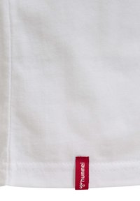 Hvid bomulds t-shirt med et rødt mærke ved kanten med brandnavnet "hummel." Glat tekstur og enkelt design.