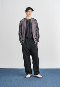 Pilkos spalvos sportinis švarkas su juodomis juostelėmis, derinamas su juodomis kelnėmis. Baltos sportinės bateliai su pilkais akcentais. Juoda kepurė puikiai užbaigia aprangą.