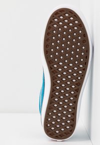 Podešev boty s hnědou gumovou plochou se vzorkem ve tvaru diamantů a bílými bočními hranami. Modrý textilní svršek připevněný vzadu.